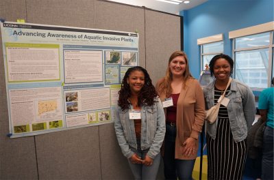 A group of 3 students smile next to a scientific poster presentation.